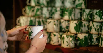 person holding a mug in front of a stack of printed mugs