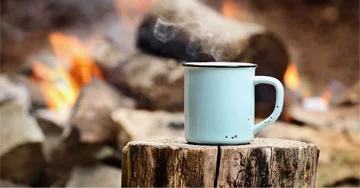 mug sitting on a log in front of a campfire