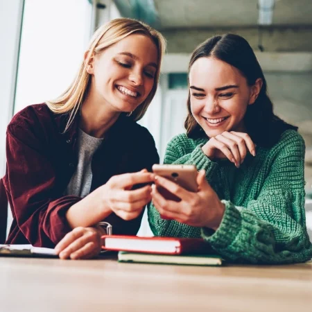 Two friends smiling while looking at a cell phone.