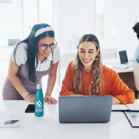 Two smiling work teammates looking at a laptop screen