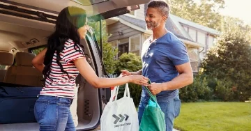 Two people unloading groceries from the car with tote bags.