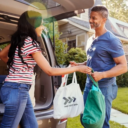 Two people unloading groceries from the car with tote bags.