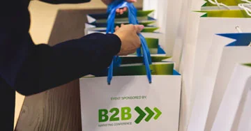 A row of gift bags that are imprinted with, Event sponsored by: B2B Marketing Conference.