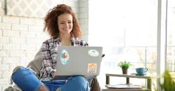 Smiling person typing on a laptop adorned with branded stickers.