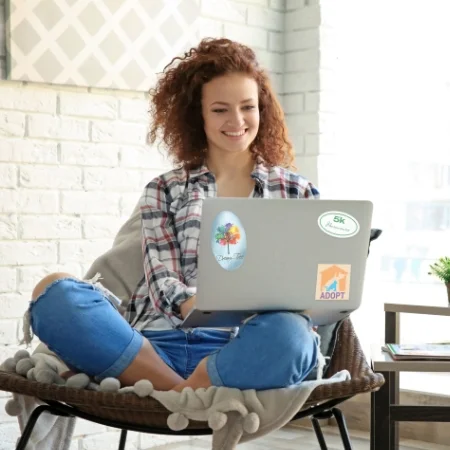 Smiling person typing on a laptop adorned with branded stickers.