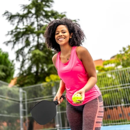 Smiling person serving a pickleball.