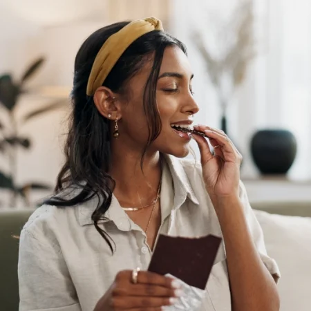 Person is taking a bite of a chocolate bar with their eyes closed.