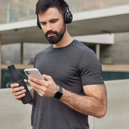 Man listening to music with headphones on while holding his phone and water bottle