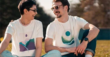 two people wearing printed t-shirts sitting on grass