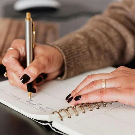 Crop woman writing down notes in diary