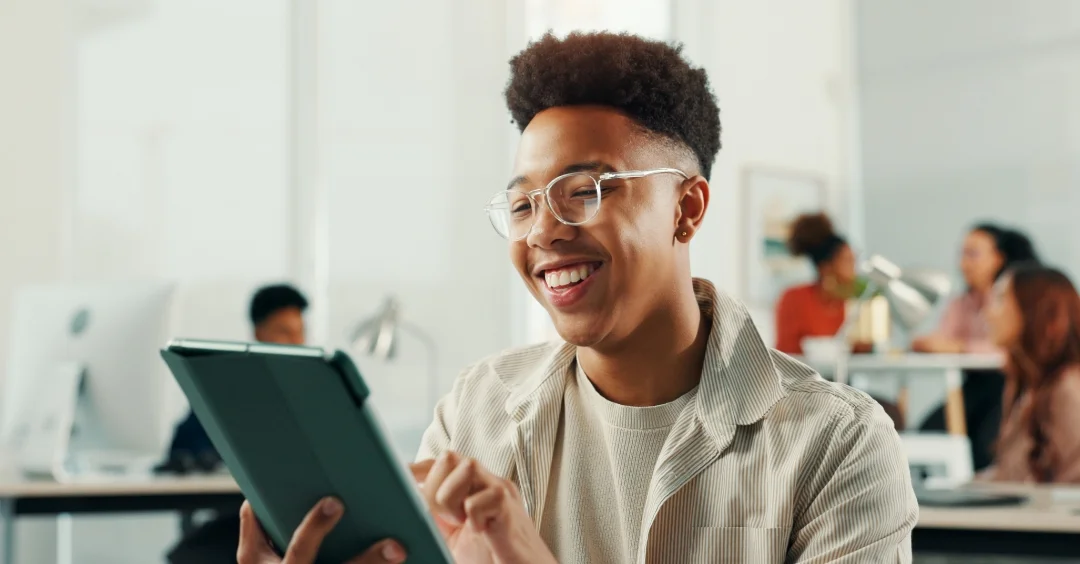 Smiling person working on a tablet in an office setting.