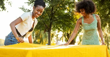 Two women outside putting a table cover on a table