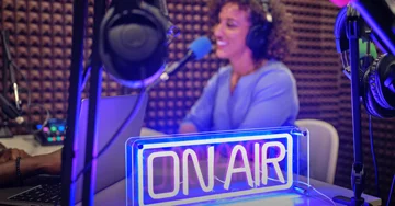 A woman at a radio station with an on air neon sign lit up