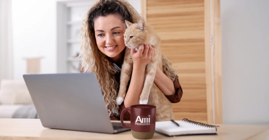Smiling person holding her cat up to her laptop screen.