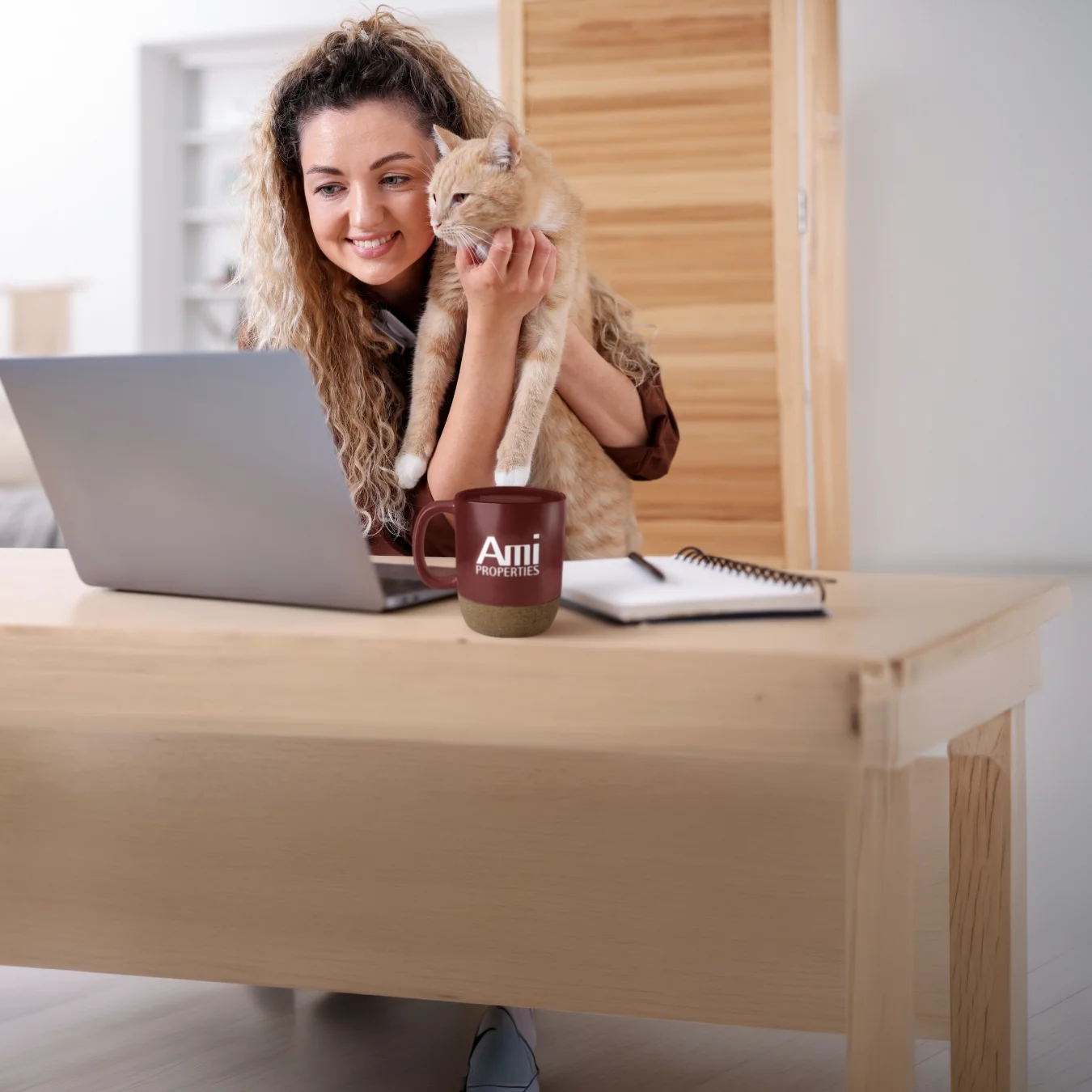 Smiling person holding her cat up to her laptop screen.