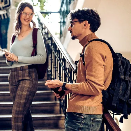 Group of students talking in a stairwell with backpacks on.