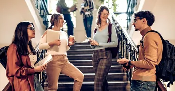 Group of students talking in a stairwell with backpacks on.
