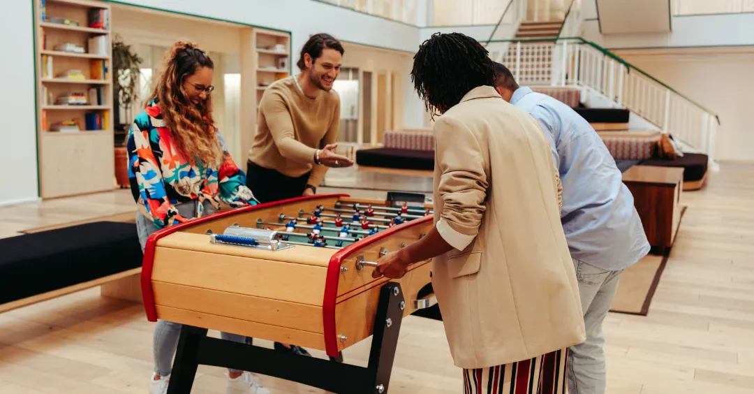 Group of teammates playing a game of foosball in an office setting.