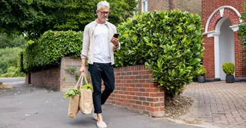A man walking home with groceries in a tote