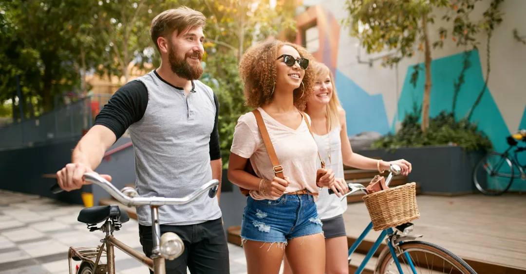 Group of three people walking downtown, two of them are pushing bikes.