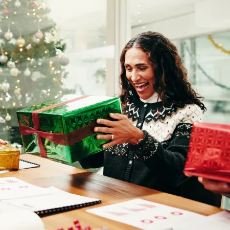 Coworkers laughing and talking while opening holiday gifts at the office.