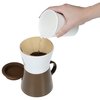 a hand holding a white shaker over a brown and white cup