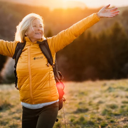 A person with her arms outstretched in a field wearing a logoed jacket