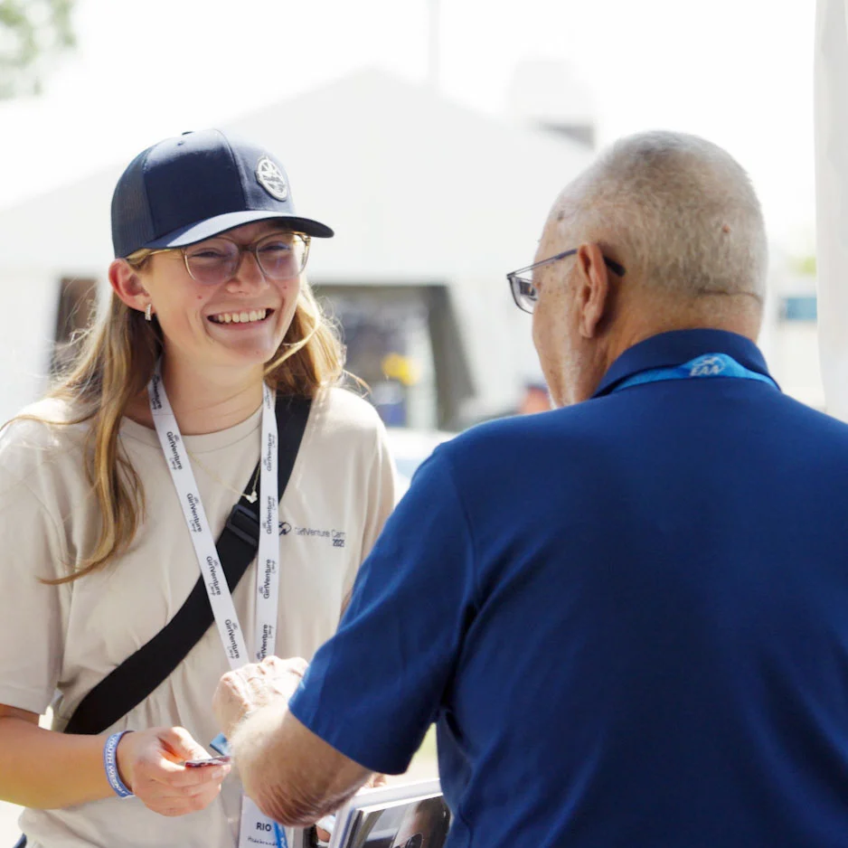 person wearing a hat and lanyard talking to another person