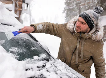 A person using a brush to remove snow from a car