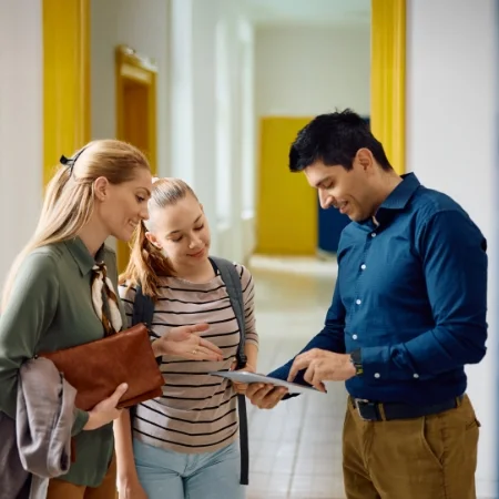 Parent and student meeting with a teacher in the hallway of a school.