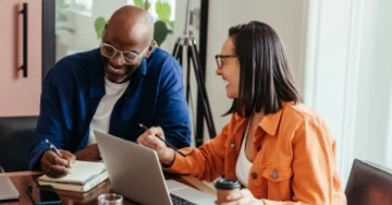 Two laughing coworkers sitting in a conference room.