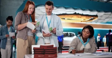 Two people wearing lanyards and working at a trade show booth.