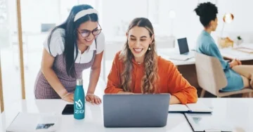 Two smiling work teammates looking at a laptop screen