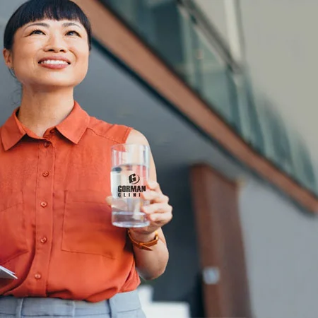 a person in a red dress holding a water bottle and a document, standing in a modern, well-lit office environment.