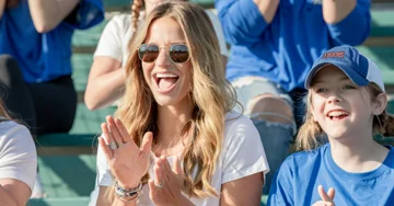 A woman and a girl in a baseball hat in a stadium cheering