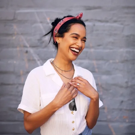 Happy person wearing a red bandana is standing in front of a gray wall.