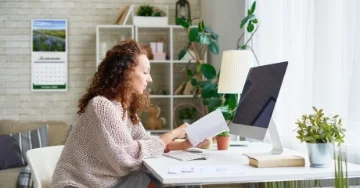 Side view of person sitting at desk in modern apartment with a branded calendar on the wall.