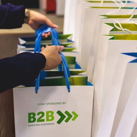 A row of gift bags that are imprinted with, Event sponsored by: B2B Marketing Conference.