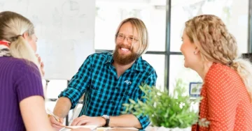 Smiling professional wearing a checked shirt with a logo and talking to teammates.