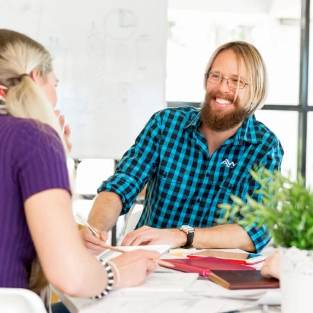 Smiling professional wearing a checked shirt with a logo and talking to teammates.