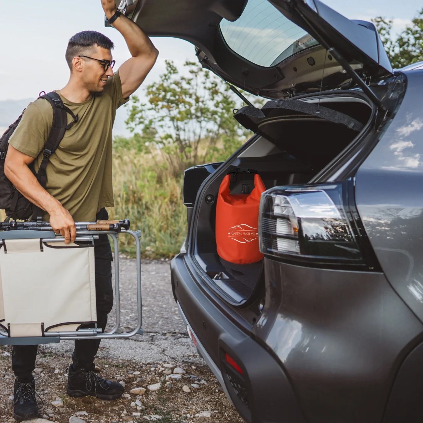 Couple loading the back of their car with chairs and camping gear. A red safety bag is sitting in the trunk.