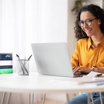 Smiling person sitting down at a desk typing on their laptop.