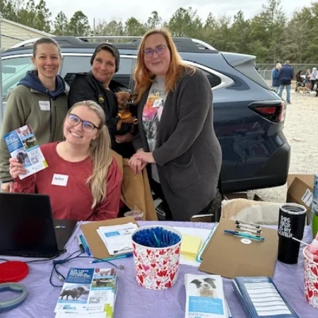 Group of smiling volunteers at an outdoor event booth.