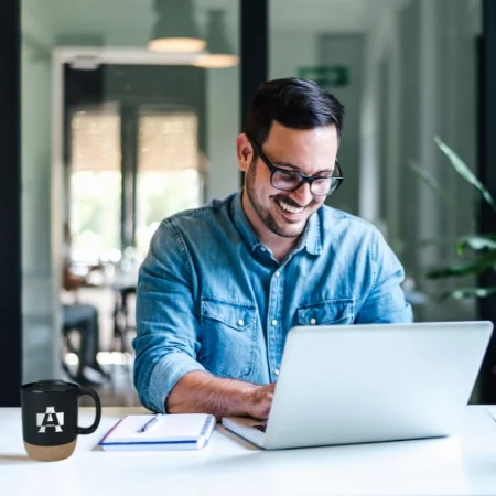 Smiling person sitting at a desk typing on a laptop.
