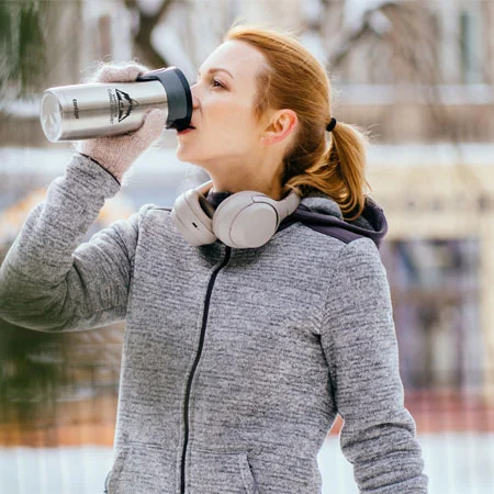 Person outside in the winter stopped during a run taking a drink from a travel mug.
