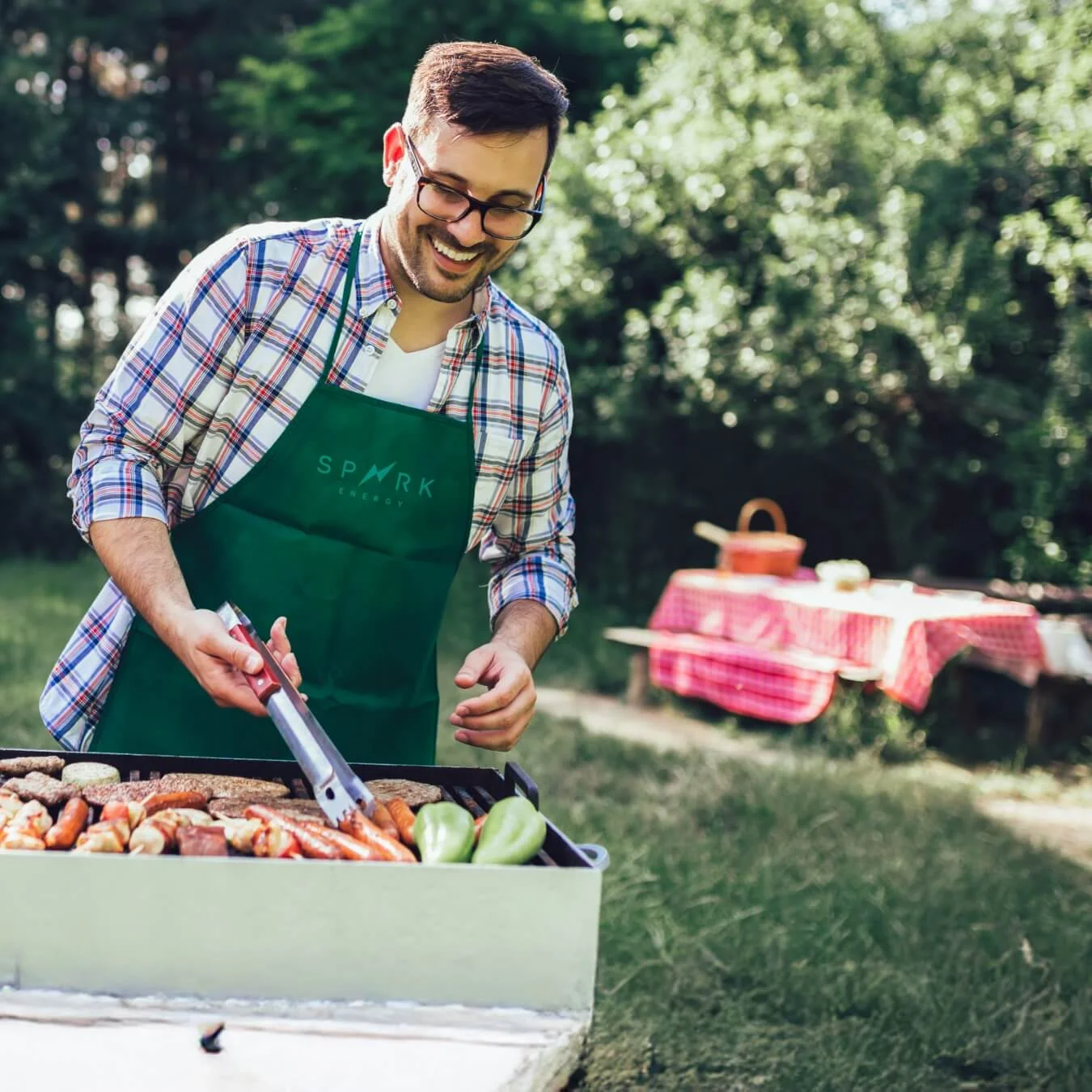 Person in a green apron standing behind the grill in a backyard.
