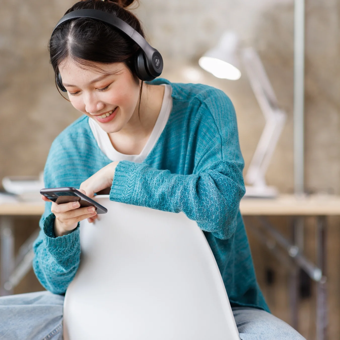 Smiling person is wearing branded headphones and looking at a smartphone.
