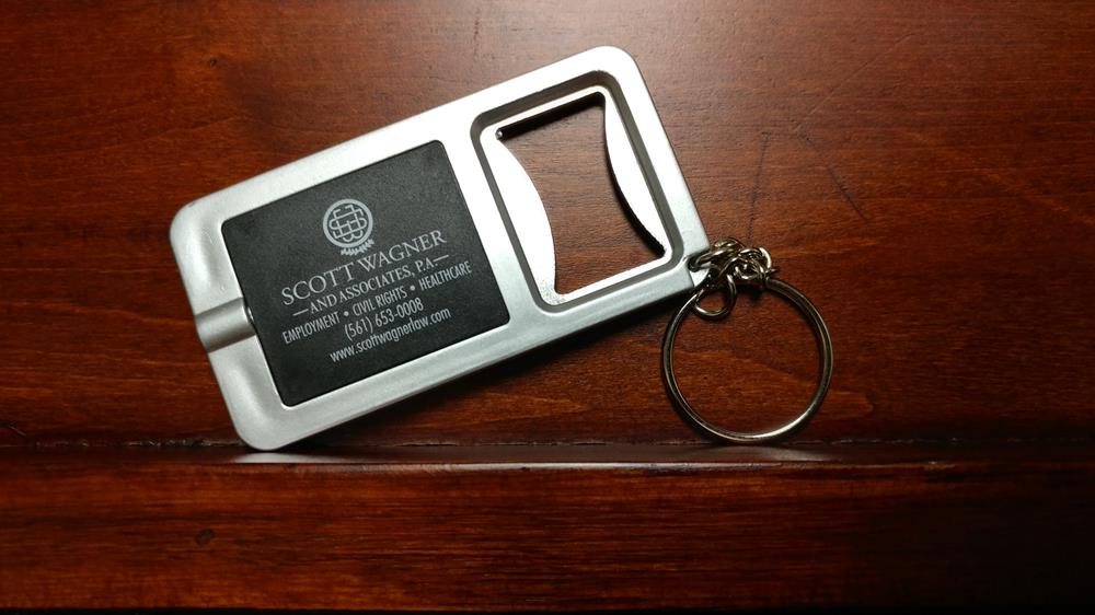Customer photo from Ashley of our Key-Light Bottle Opener - Square - 24 hr, a bottle opener on a wood surface