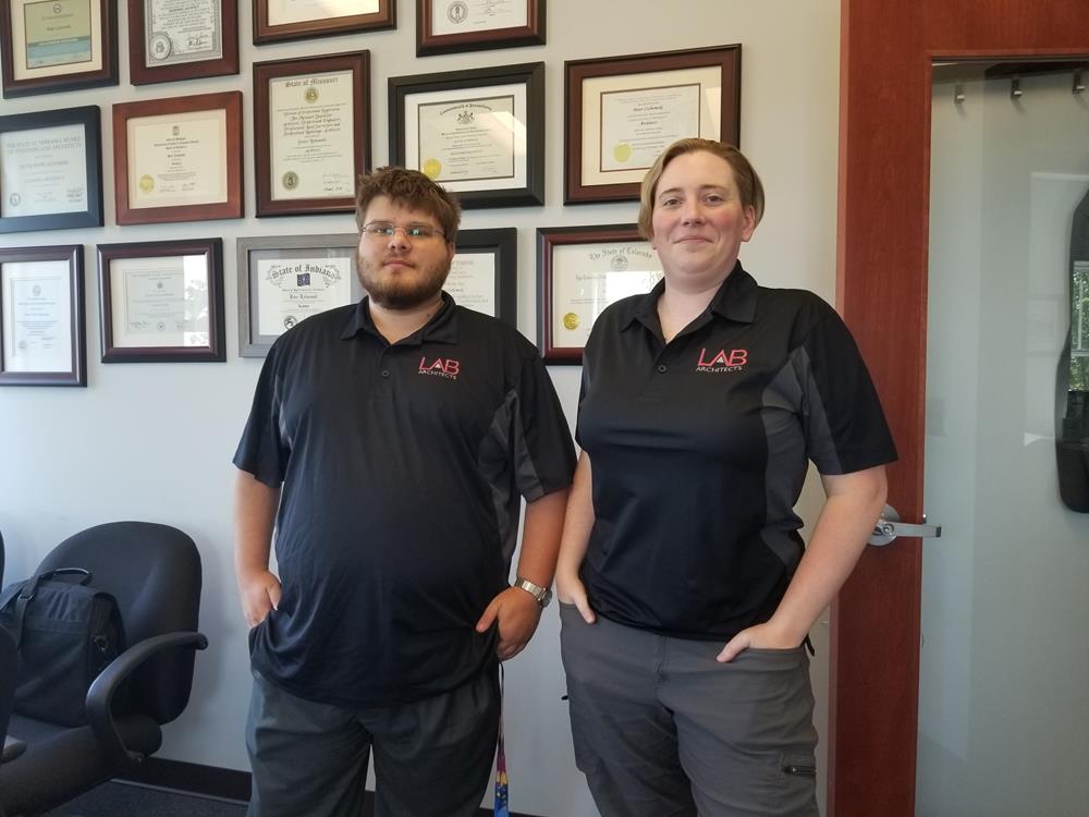 Customer photo from Peter of our Side Blocked Micropique Sport-Wick Polo - Men's - Embroidered, two people standing in front of a wall with framed pictures