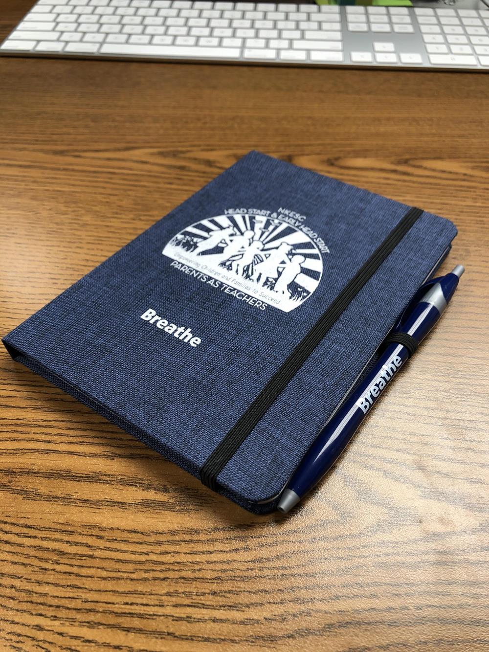 Customer photo from Rebekkah of our Javelin Pen, a blue notebook and pen on a wooden surface